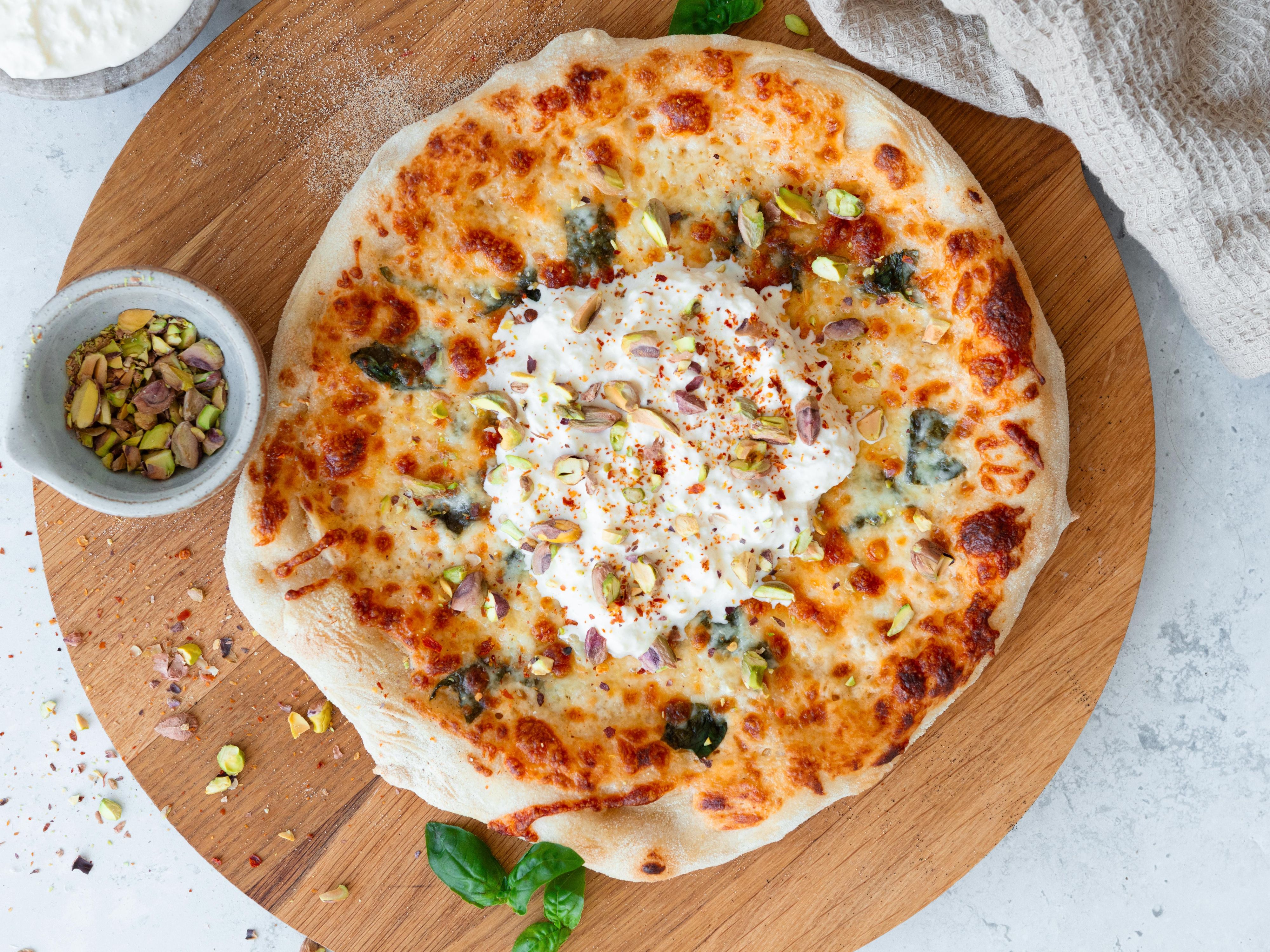 Stracciatella pizza på en rund trefjøl.