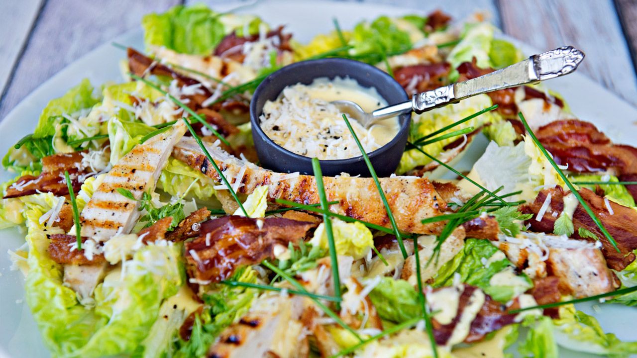 Cæsarsalat med bacon og kylling på et stort hvitt fat
