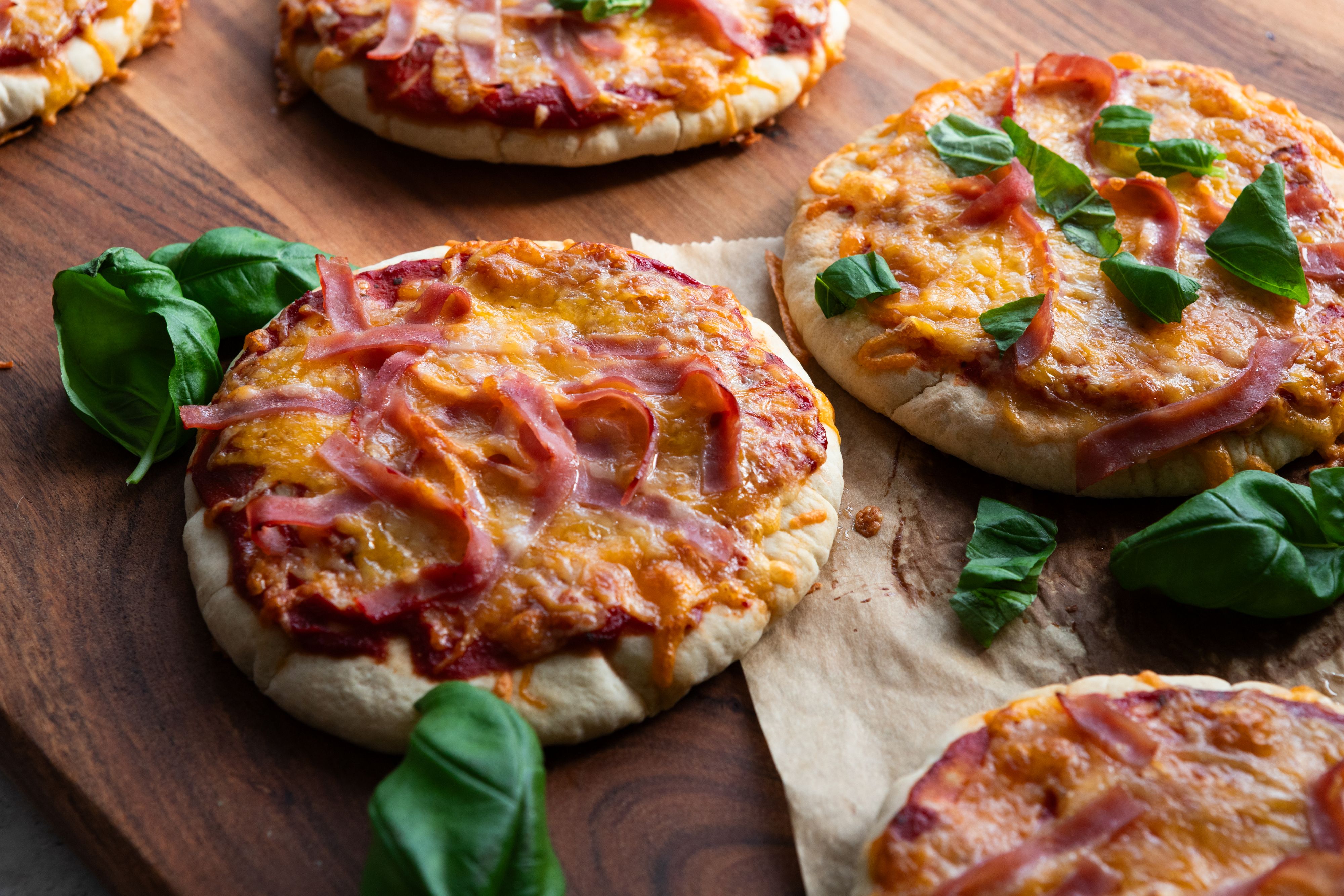 Nærbilde av pitapizzaer med ost og skinke på trefjøl