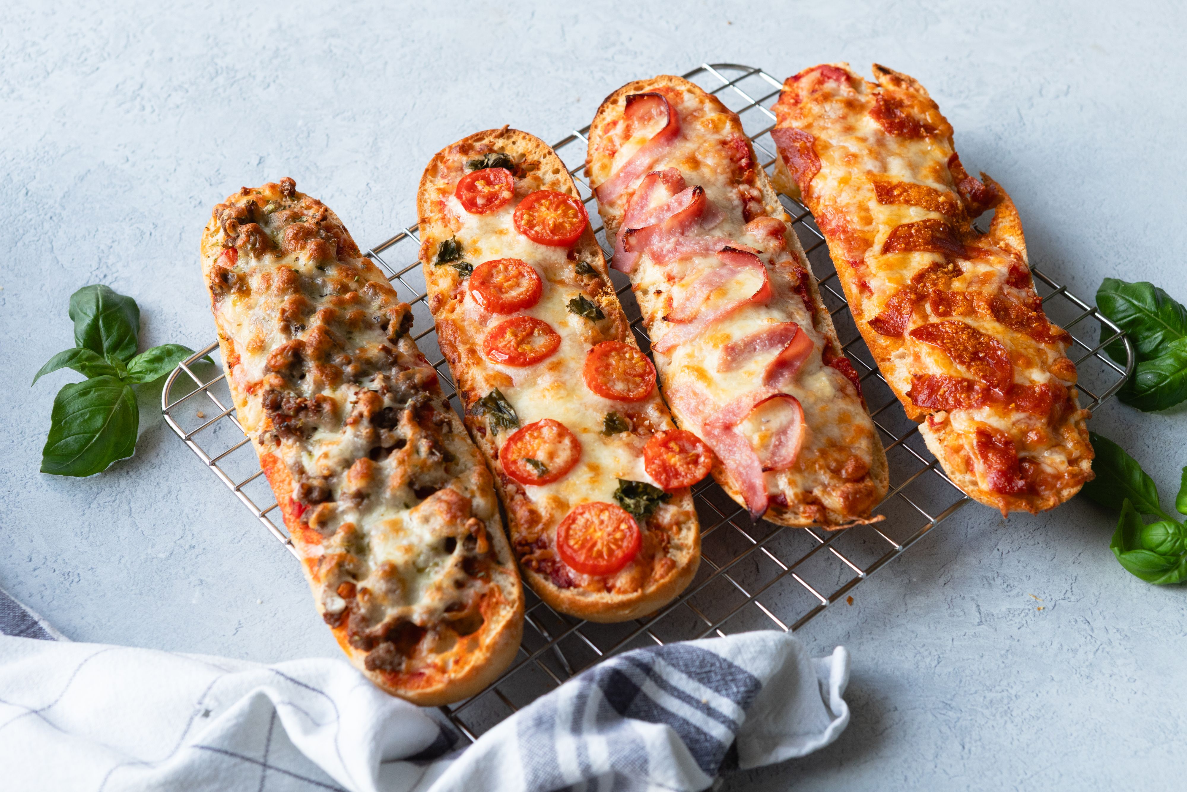 Fire halve pizzabaguetter med diverse topping på stekerist.